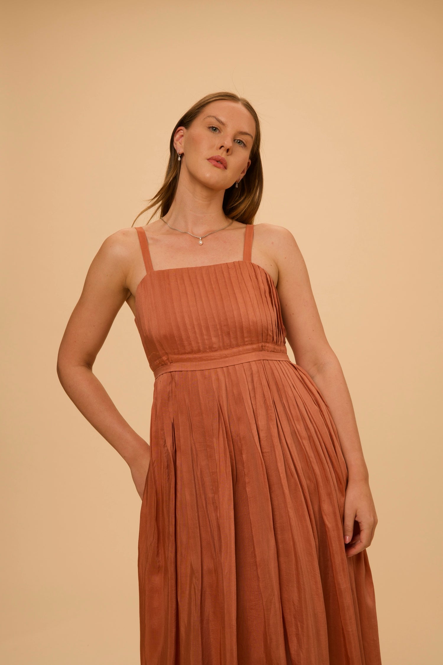 A terracotta pleated dress, photographed close, for The PRIVÉ Club.