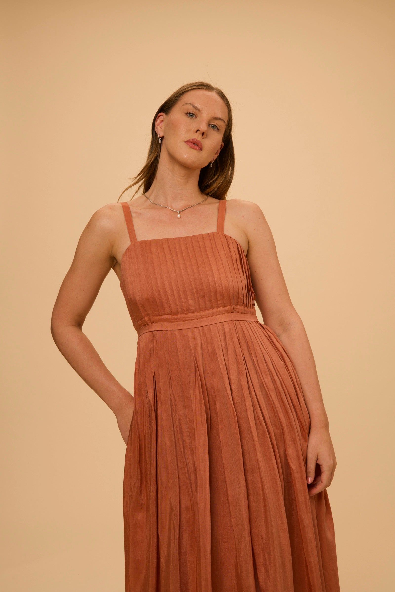 A terracotta pleated dress, photographed close, for The PRIVÉ Club.